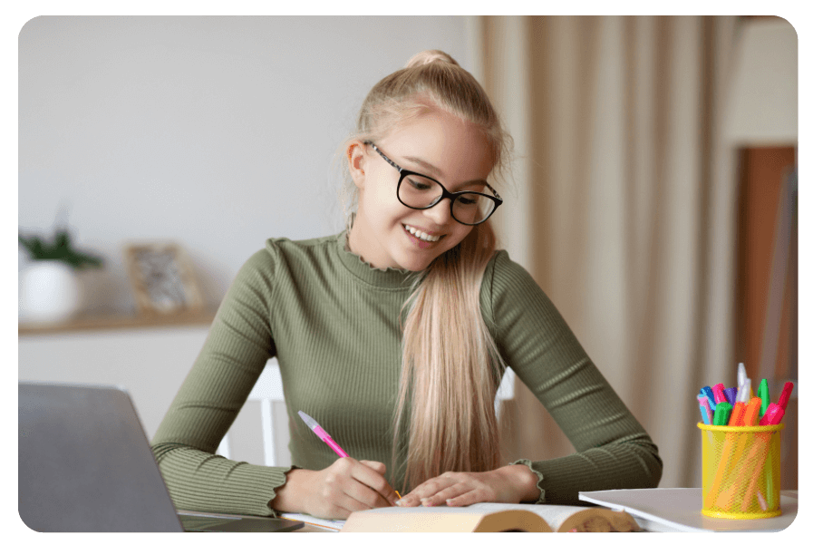 Jeune étudiante souriante faisant ses devoirs avec un ordinateur portable et des fournitures scolaires