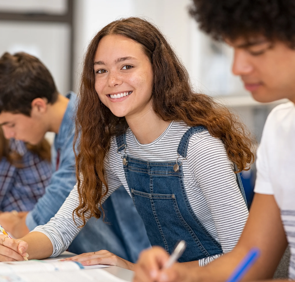 Lycéenne souriante en classe travaillant avec ses camarades, symbolisant la réussite scolaire et la motivation des étudiants