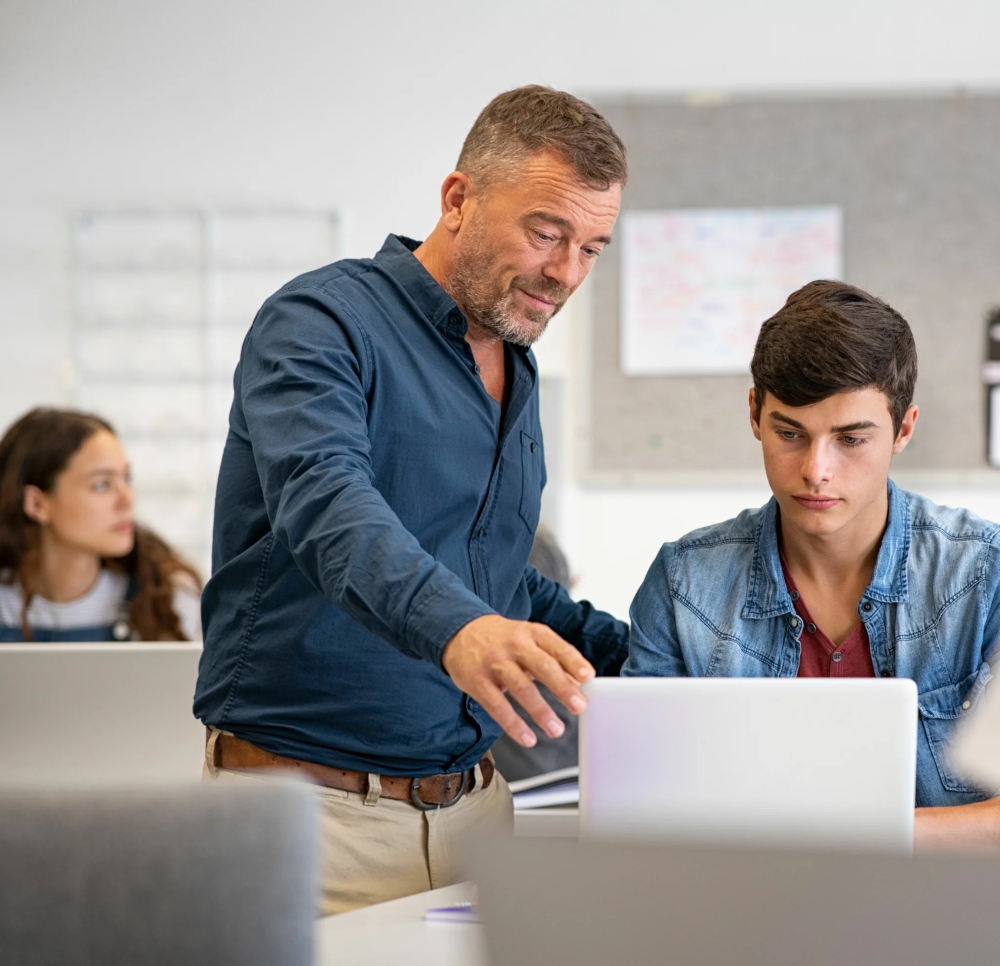Professeur aidant un élève sur ordinateur portable en classe, soutien pédagogique et apprentissage personnalisé
