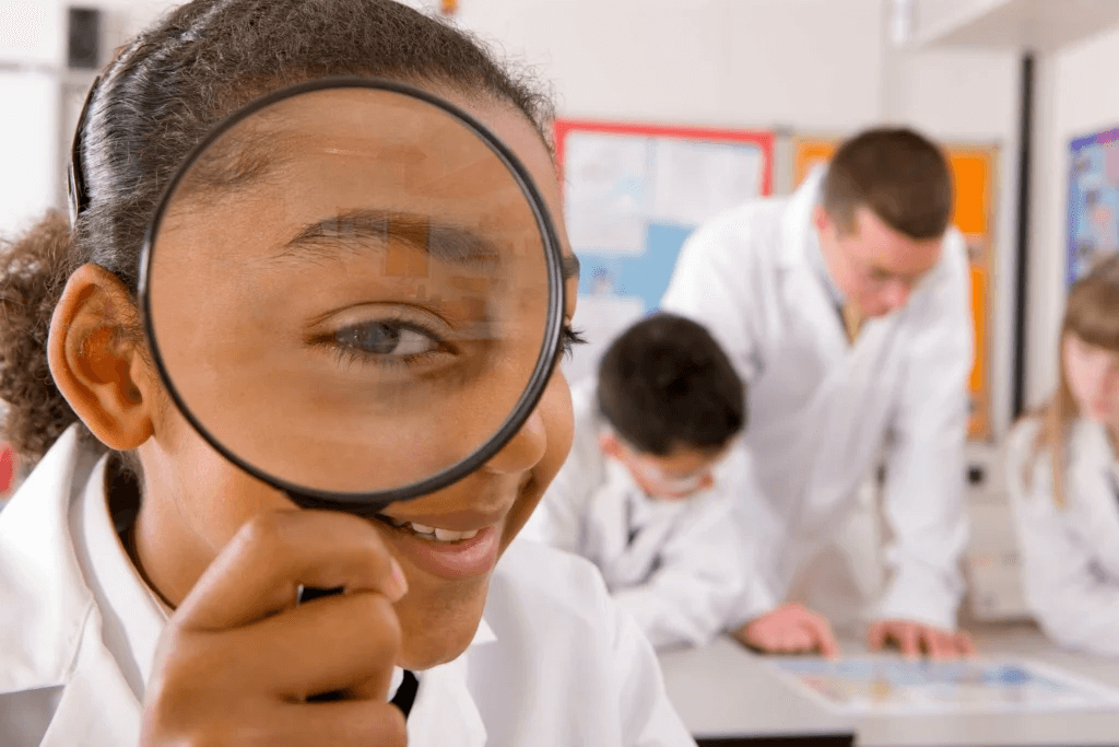 Élève en blouse blanche utilisant une loupe pour observer de près lors d’un cours de sciences, représentant l’apprentissage ludique et la découverte scientifique