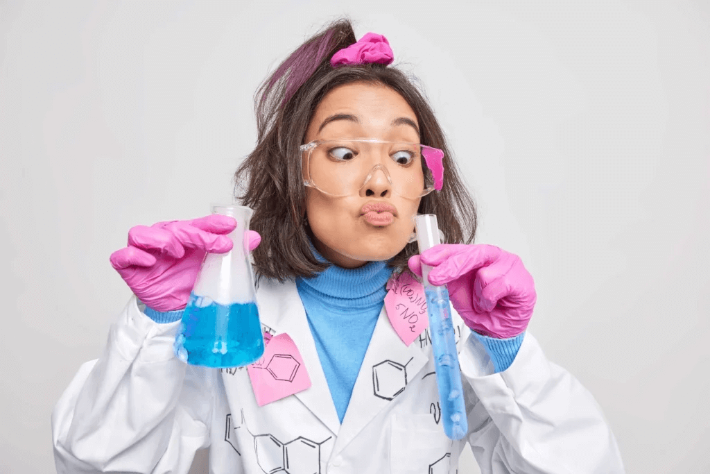 Jeune femme en blouse de laboratoire avec des gants roses et des lunettes de protection, réalisant une expérience de chimie avec un bécher et une éprouvette contenant un liquide bleu