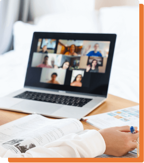 Ordinateur portable affichant une visioconférence avec plusieurs participants et cahiers ouverts sur un bureau