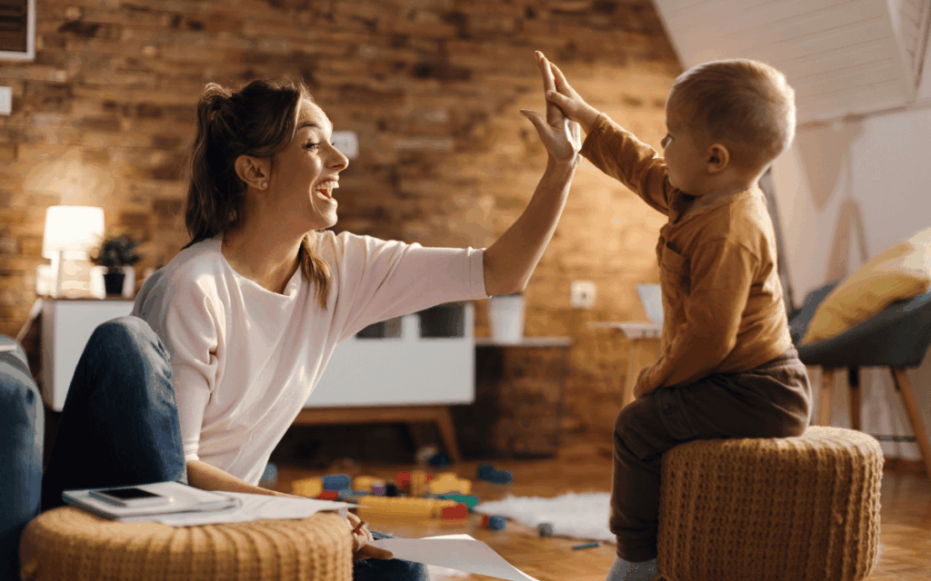 Une maman souriante fait un high five avec son enfant à la maison, illustrant l’importance du jeu et de l’interaction positive dans le développement du langage.