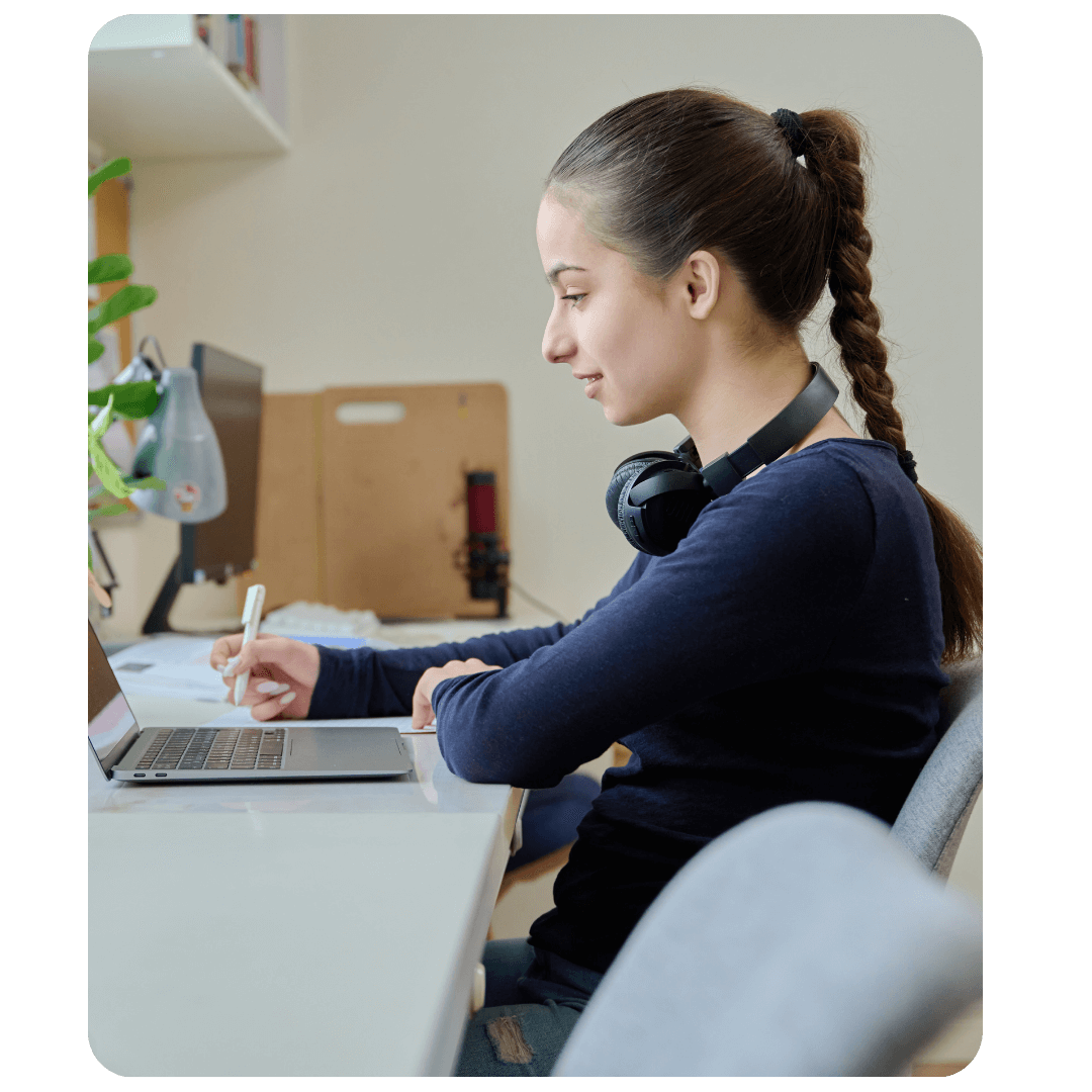 Jeune fille concentrée prenant des notes devant son ordinateur portable avec un casque autour du cou
