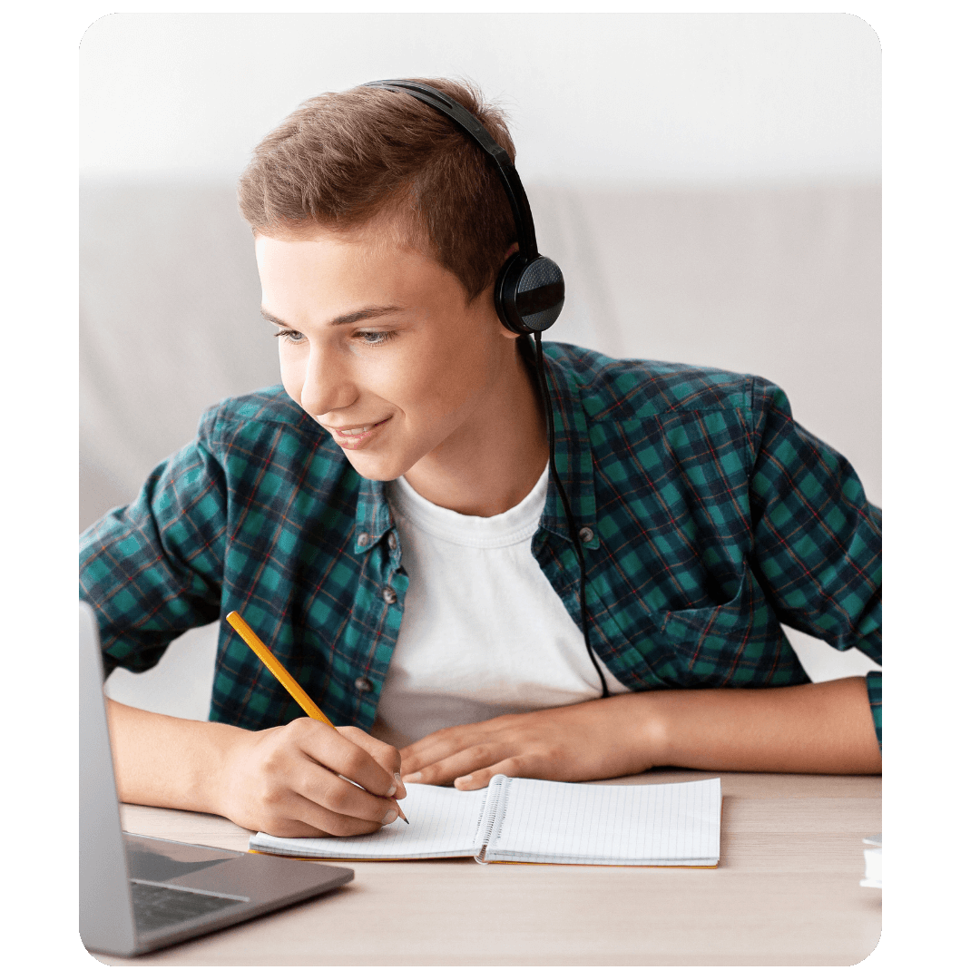 Adolescent portant un casque audio, écrivant dans un cahier devant un ordinateur portable lors d’un cours en ligne